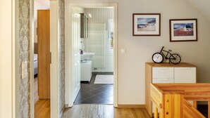 Ein Flur, der zu einem Badezimmer mit Toilette, Waschbecken und Dusche führt. An der Wand befinden sich Bilder in Rahmen, und in einem Schrank steht ein Fahrrad.