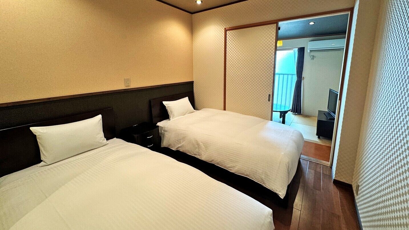 A hotel room with two beds, a wooden floor, and a sliding door leading to a balcony.