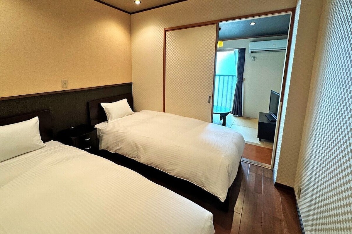 Quarto de hotel com duas camas, piso de madeira e porta deslizante para uma varanda.