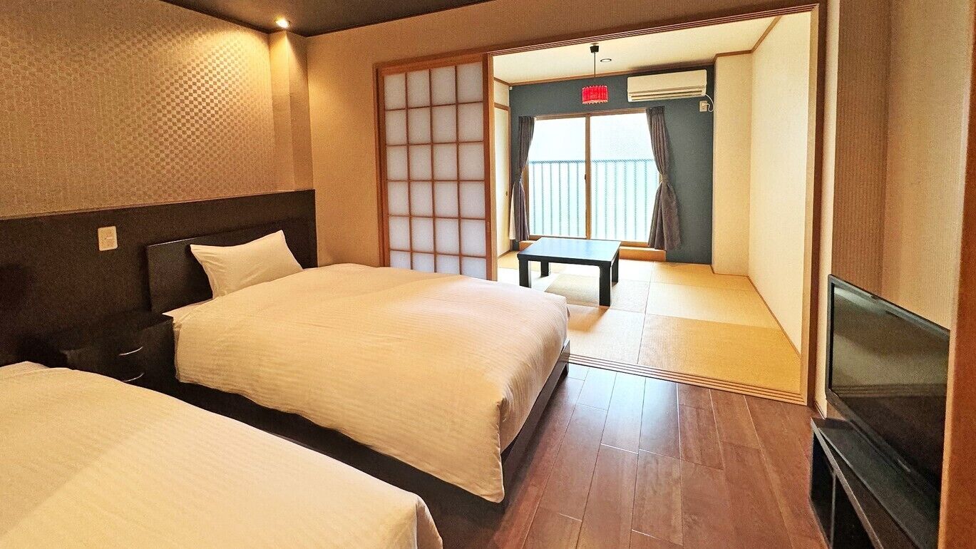 A hotel room with two beds, a TV, a sliding door leading to a balcony, and a small table.