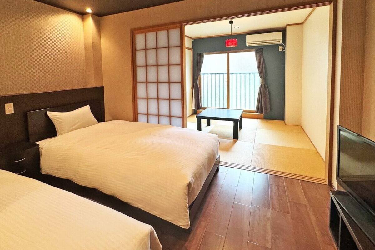 Quarto de hotel com duas camas, televisão, porta de correr para uma varanda e uma pequena mesa.