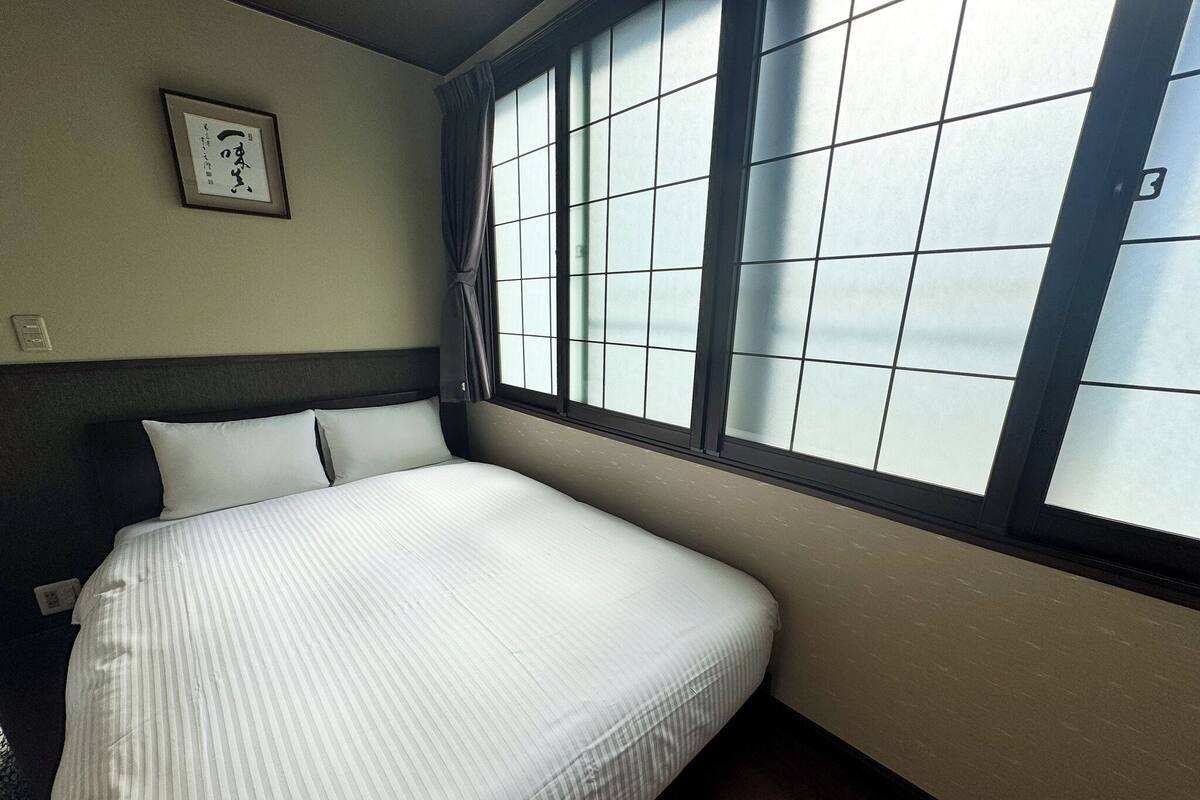 Cama bem arrumada com colcha listrada, um quadro na parede e uma janela com vista para o exterior.