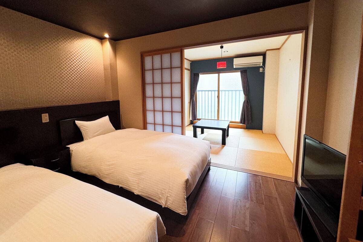 Quarto de hotel com duas camas, televisão e porta de correr para uma varanda.