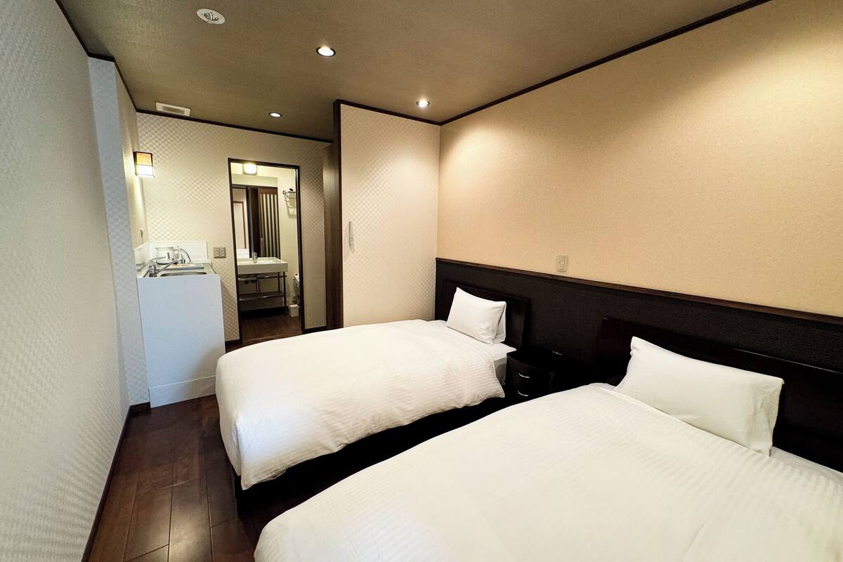 Quarto de hotel com duas camas, banheiro e uma pequena cozinha.