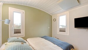 Une chambre avec deux lits, une télévision et deux fenêtres équipées de stores.