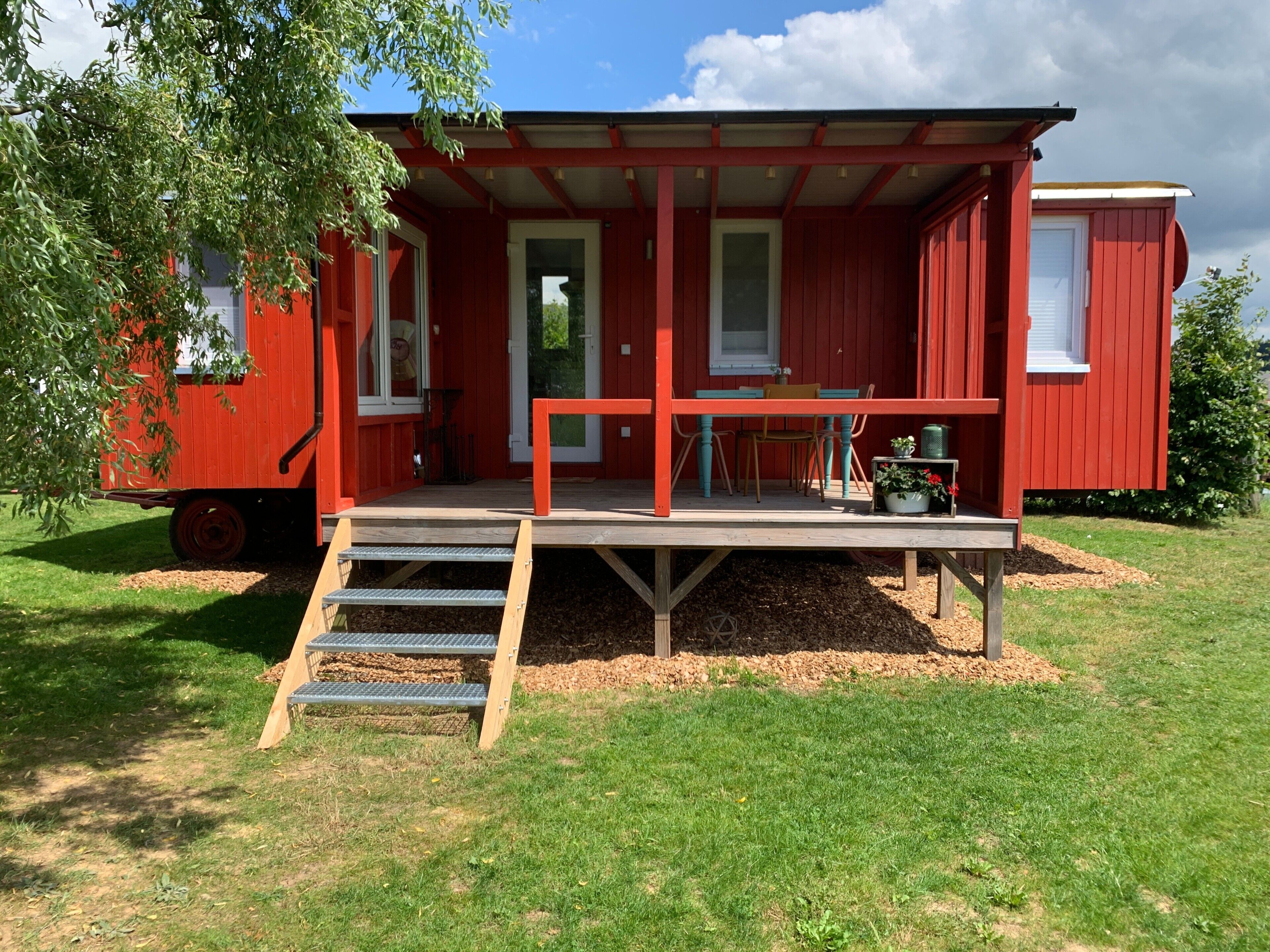 A red mobile home with a porch, a table, and chairs.