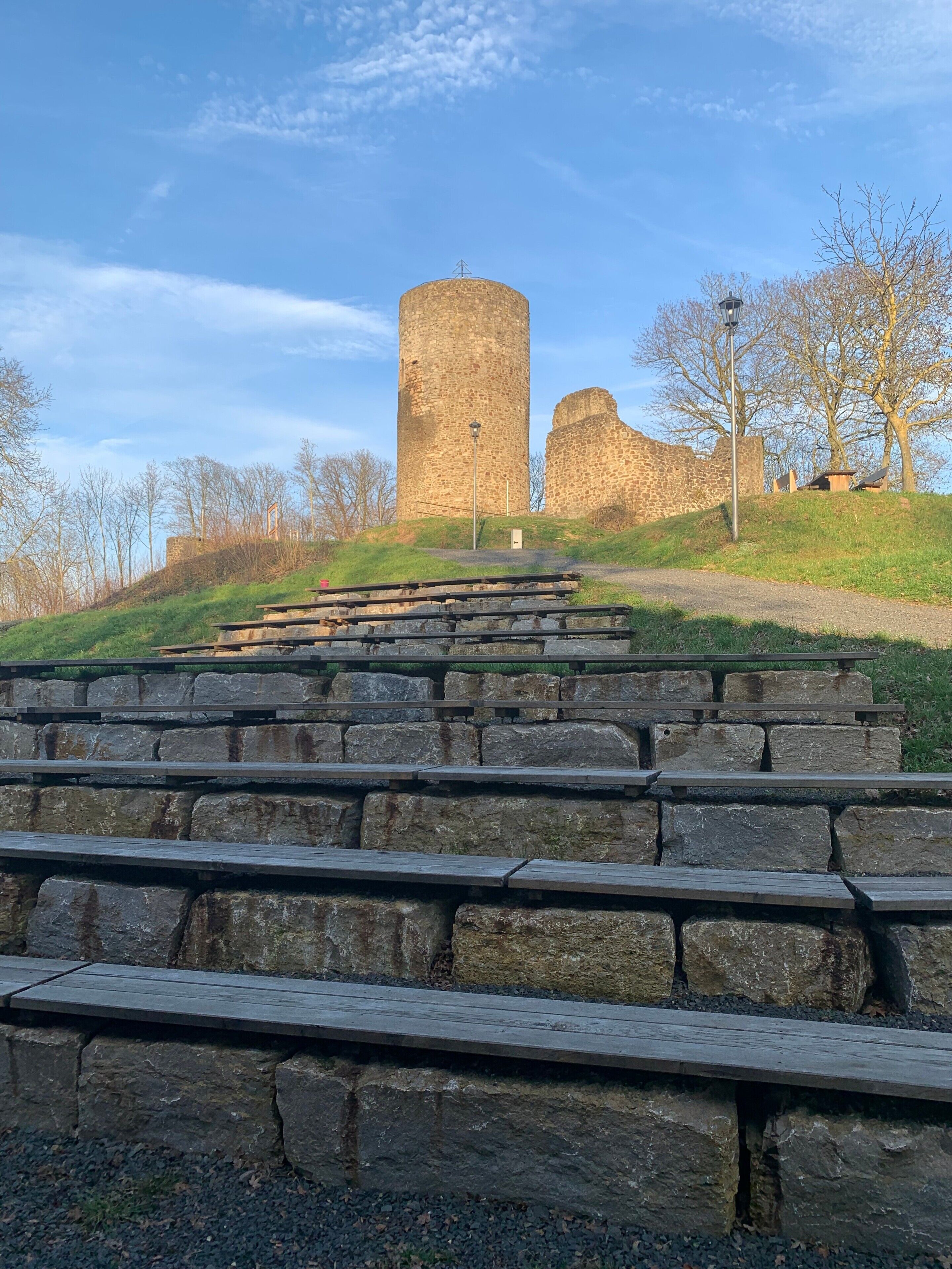 A stone staircase leading up to a historic tower with a flat top, surrounded by trees and a clear sky.