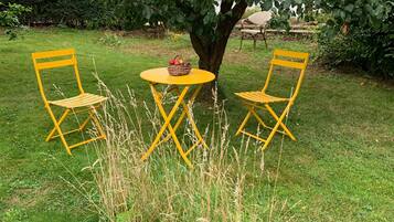 Een tuin met twee gele stoelen en een kleine tafel onder een boom.