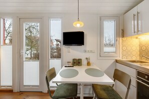 A kitchen with a TV, a dining table with chairs, and a window with blinds. - 'Tiny House Im Grünen' with Private Terrace and Private Garden (Jesberg)