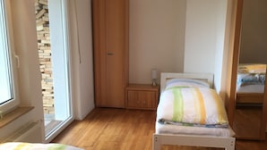 Un dormitorio con dos camas, un armario de madera, una mesita de noche con una lámpara y una ventana con vista a un muro de piedra.