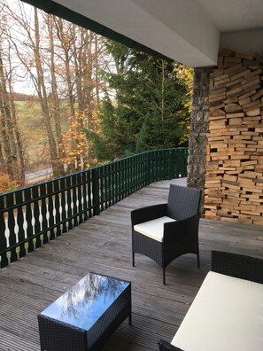 A covered outdoor seating area with wicker furniture, a glass-top table, and a stone wall.
