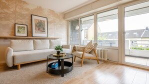 Un salón con sofá, una mesa de centro, una silla y ventanas amplias.