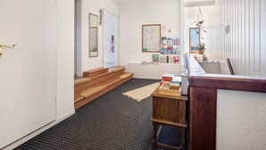 Un pasillo con una escalera de madera, una mesita con libros, un mapa en la pared y una planta en maceta.