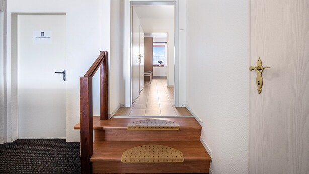 Un pasillo con una escalera de madera, una puerta con un letrero y vista a una habitación con balcón.