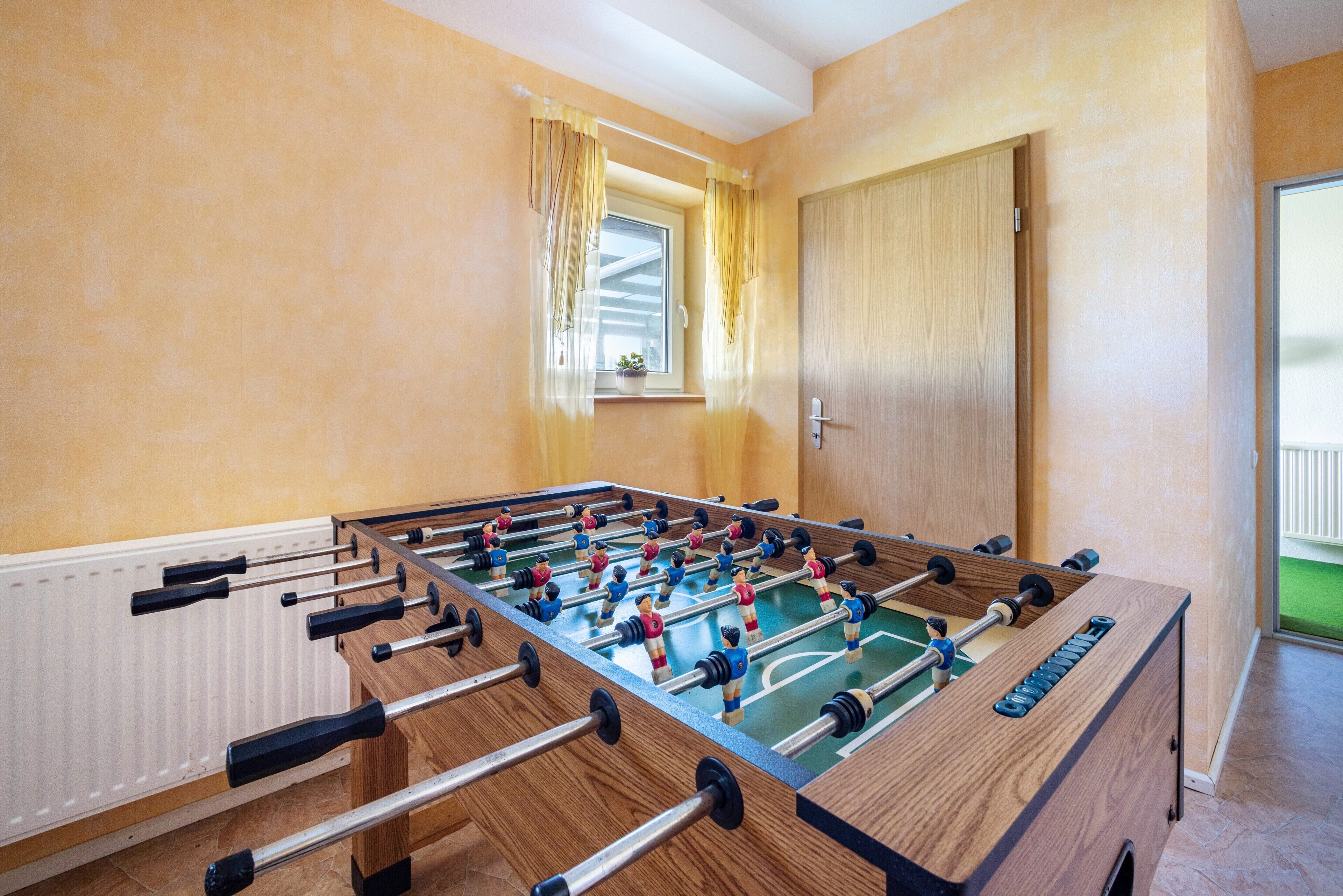 Una mesa de fútbolín en una habitación con ventana, puerta de madera y radiador.
