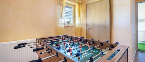 Una mesa de fútbolín en una habitación con ventana, puerta de madera y radiador.