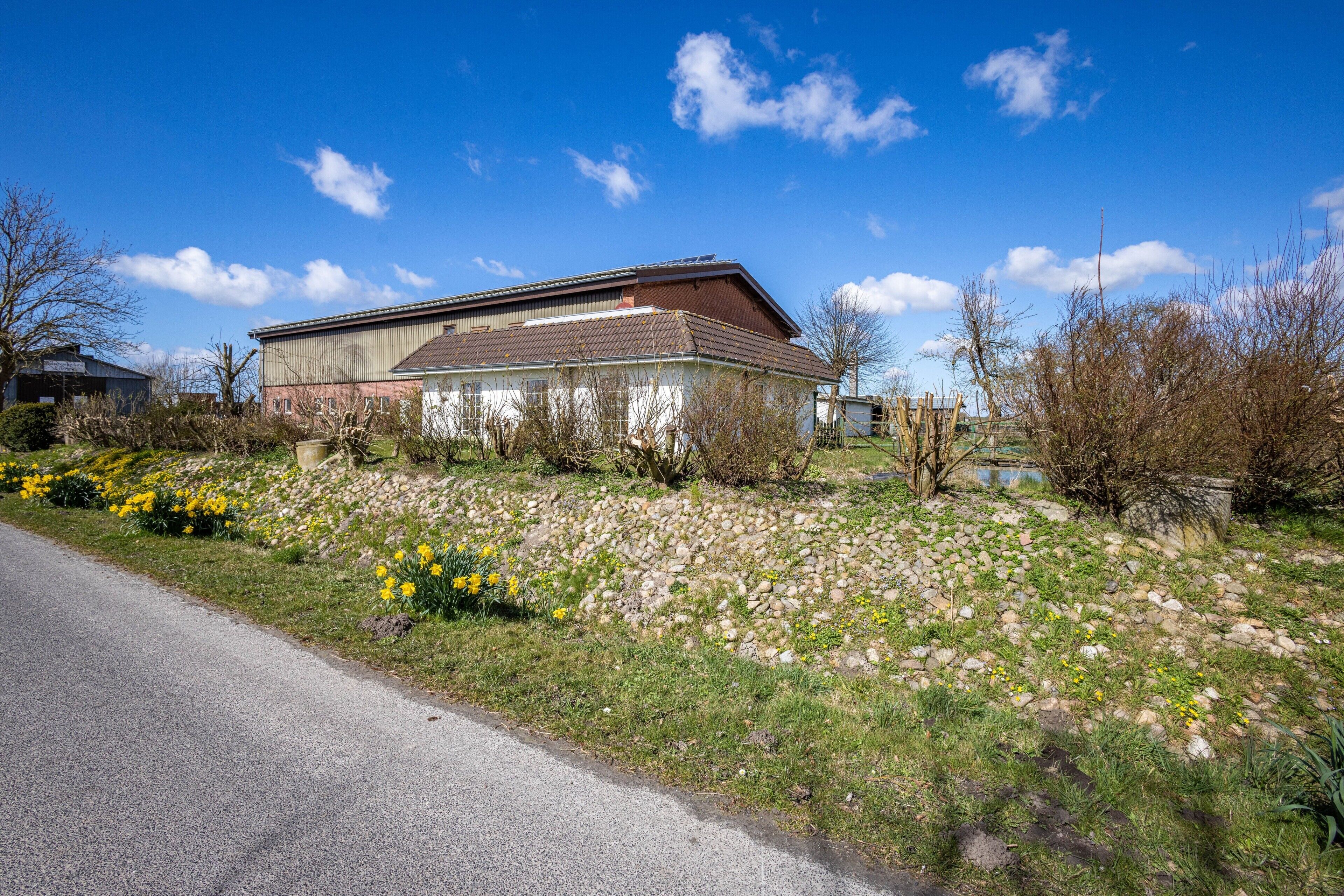 Ein Gebäude mit einem geneigten Dach, umgeben von einem Garten mit gelben Blumen und einem Kiesweg.