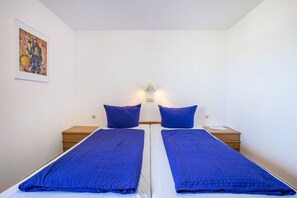 Ein Doppelbett mit blauer Decke, zwei Nachttische, eine Wandleuchte und ein gerahmtes Bild.