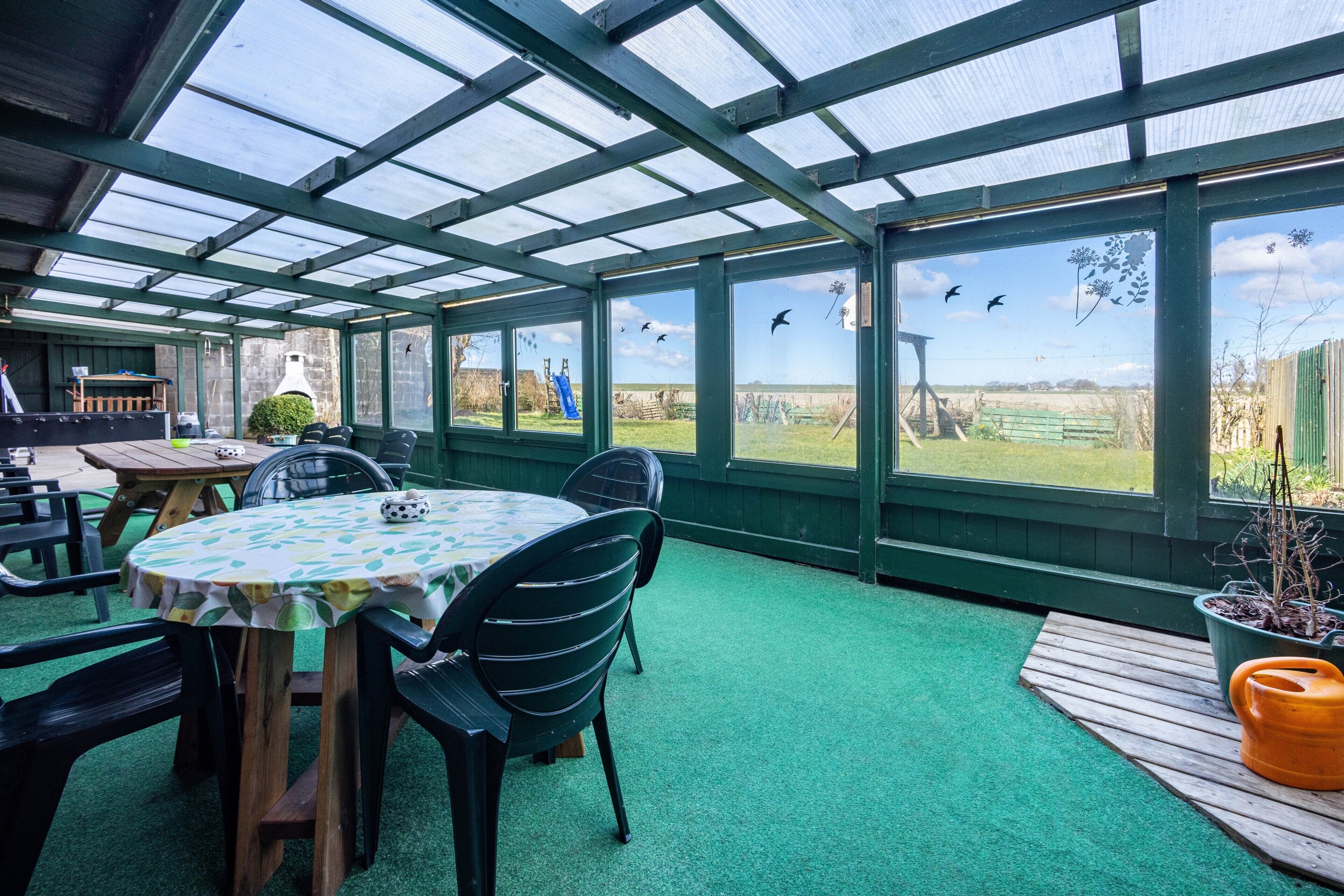 Ein überdachter Patio-Bereich mit Tisch und Stühlen, einer hölzernen Bank und Blick ins Freie.