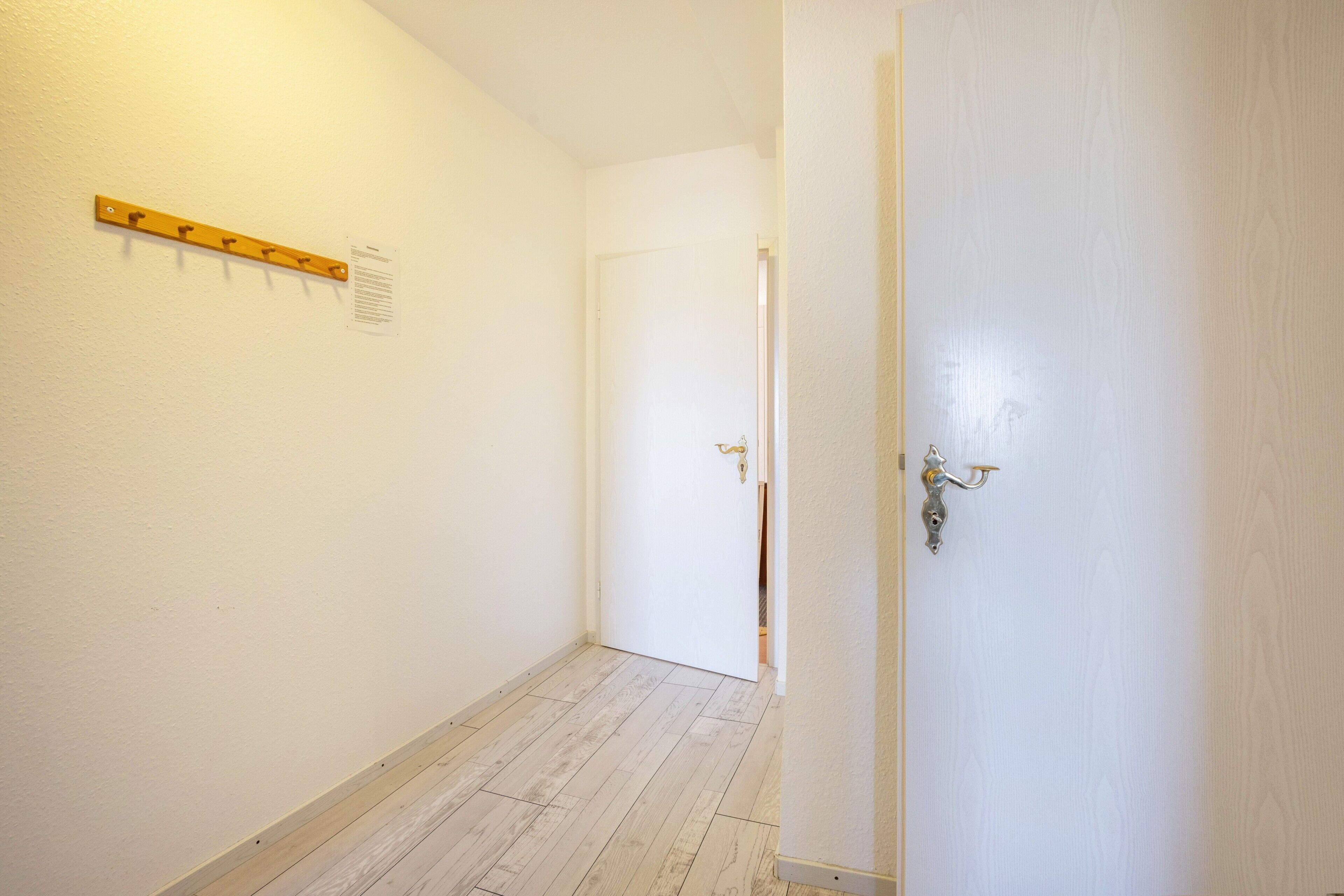 A hallway with a coat rack, a door with a handle, and a wooden floor.