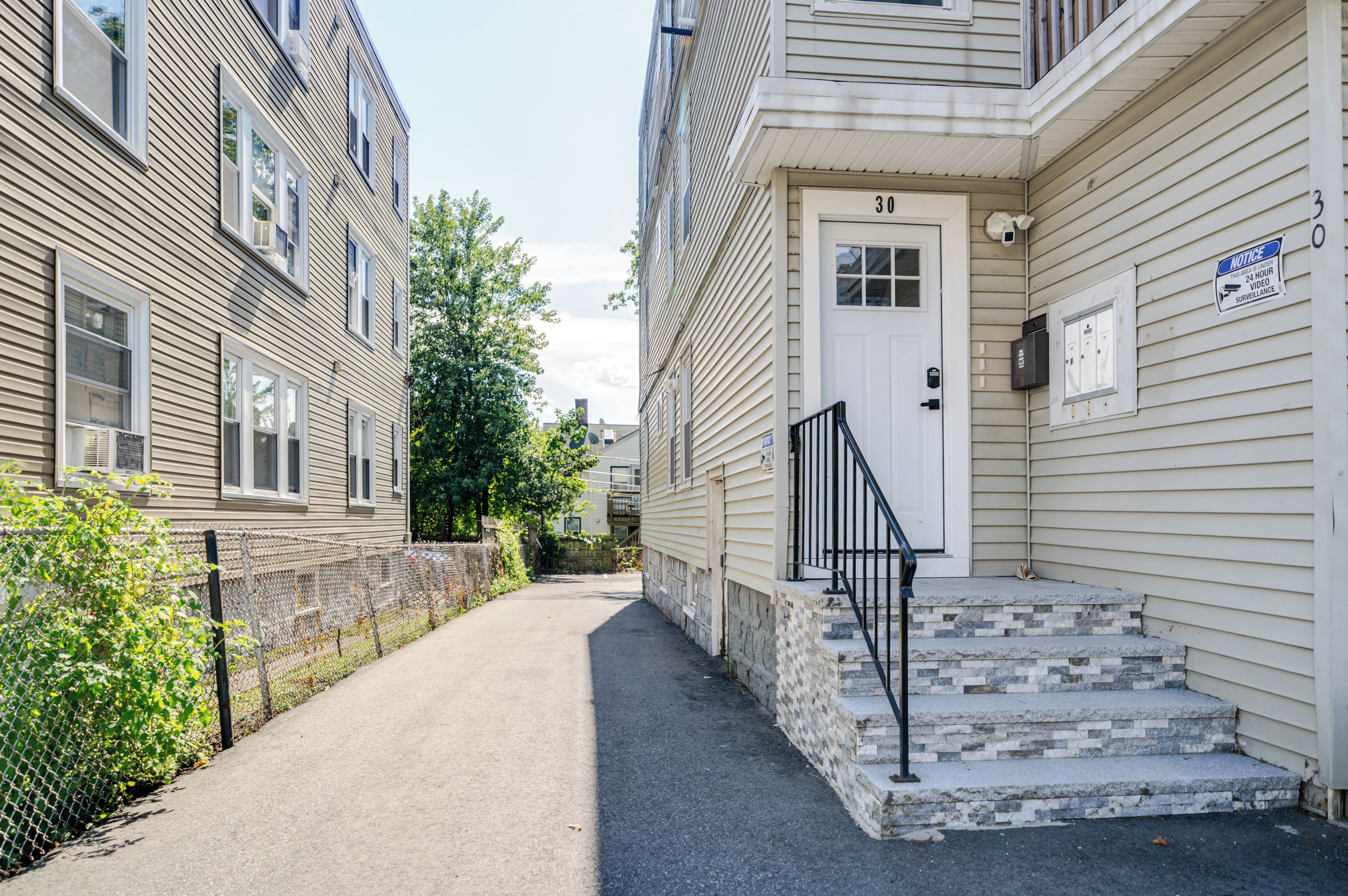 A narrow alleyway between two buildings with a metal fence on one side and a door with steps on the other.