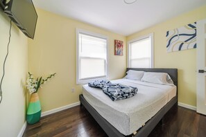A bedroom with a bed, two windows, a painting, and a vase with flowers. - Spacious 4BR Boston 1st-floor Apt w/ Free parking • Pet-friendly 301 (Boston)