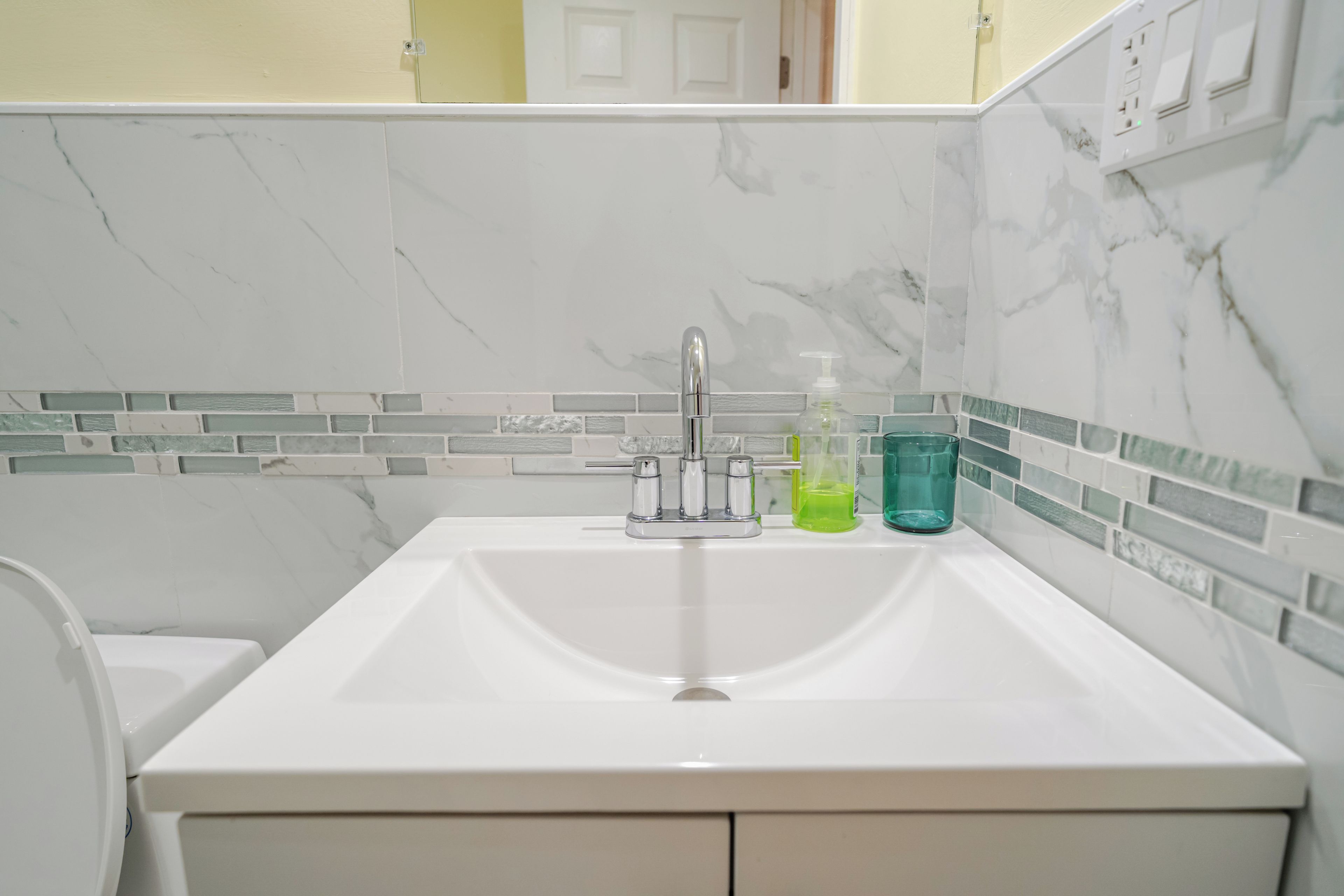 Une salle de bain avec un lavabo blanc, un miroir et un mur recouvert de carreaux.