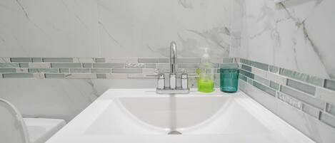 Une salle de bain avec un lavabo blanc, un miroir et un mur recouvert de carreaux.