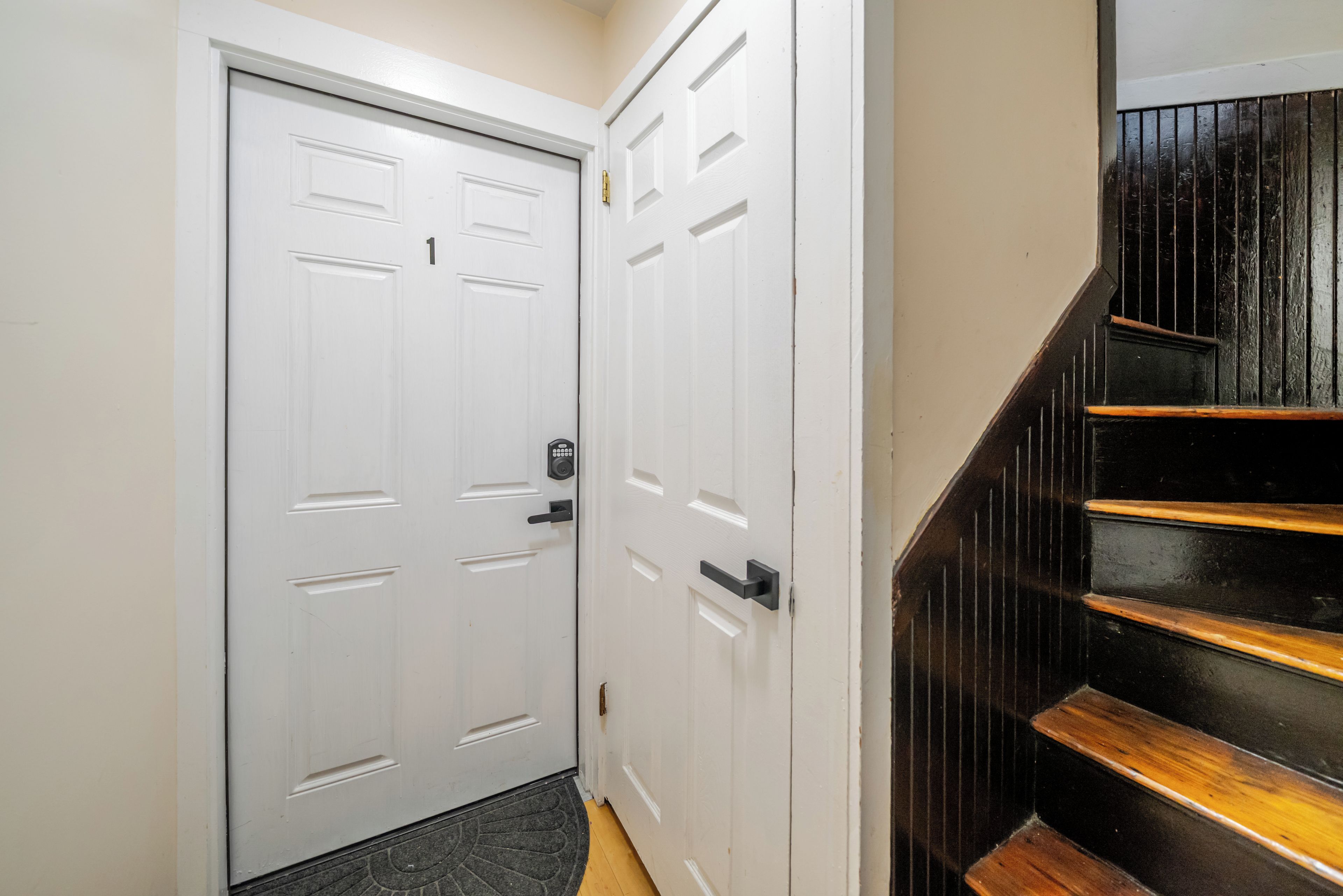 A hallway with a white door, a black door, and a wooden staircase.