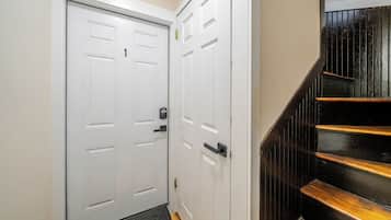 A hallway with a white door, a black door, and a wooden staircase.