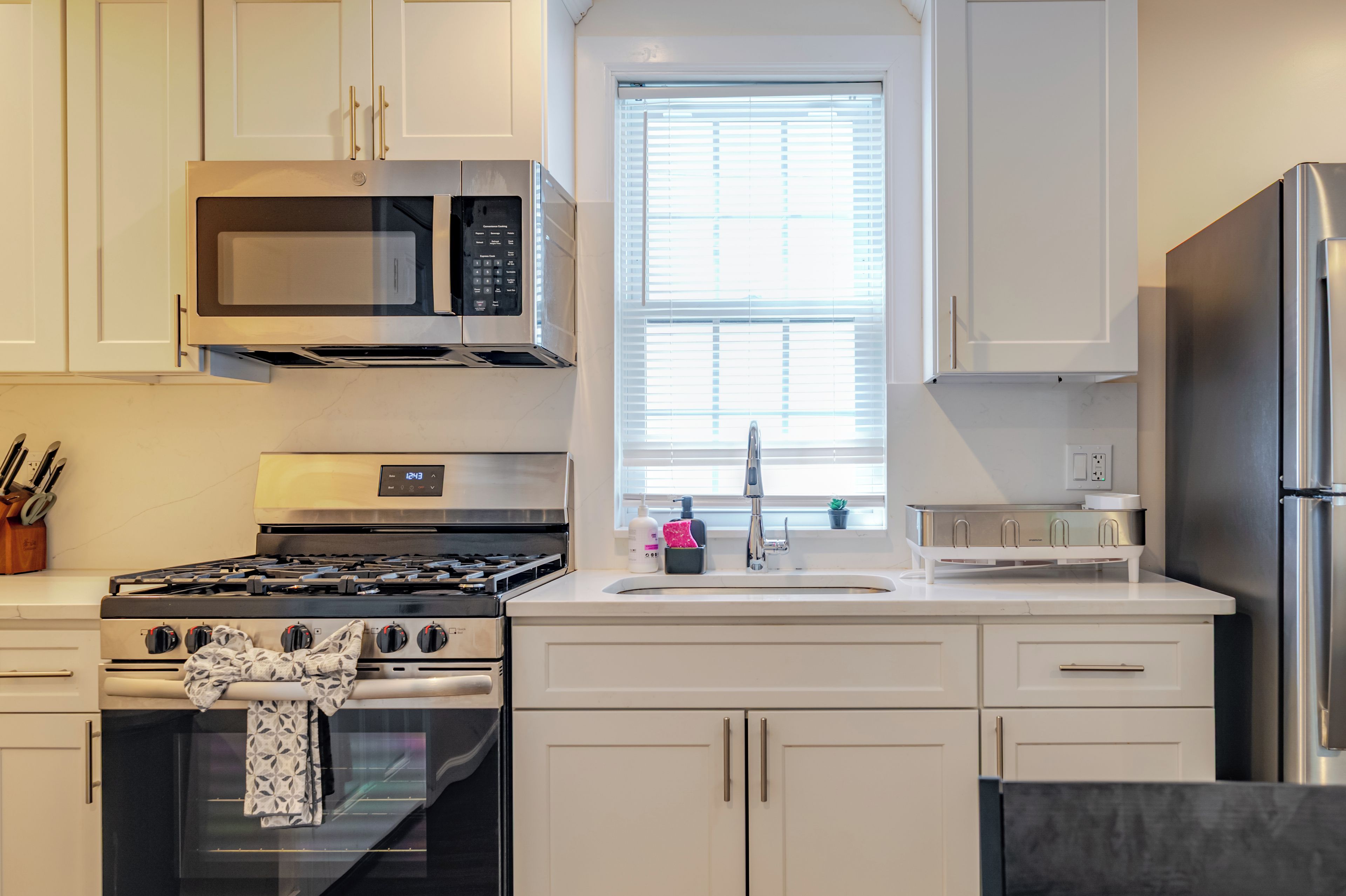 A modern kitchen with stainless steel appliances, white cabinetry, and a window with blinds.