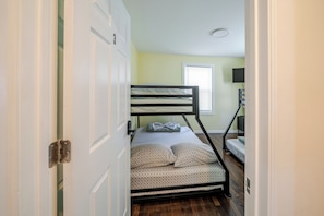 Una cama litera en una habitación con puerta, ventana y escritorio con lámpara.