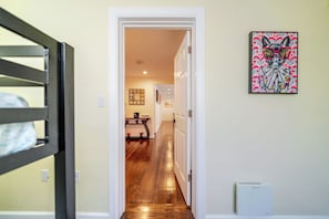 Un couloir avec un plancher en bois, une porte blanche et un tableau encadré accroché au mur.