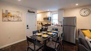 A modern kitchen with white cabinets, a stainless steel refrigerator, and a dining table set for four.