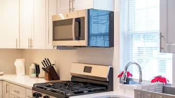 A kitchen with white cabinets, a stainless steel stove, a microwave, and a window with blinds.