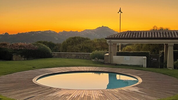 A wooden deck surrounding a circular pool with a pergola and a street lamp in the background. - Gardenia Luxury (Palau)