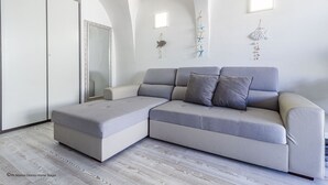 A modern living room with a grey sectional sofa, a large mirror, and decorative wall hangings. - Gardenia Luxury (Palau)