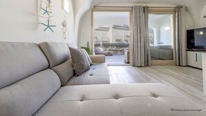 A modern living room with a sofa, a television, and a view of a courtyard. - Gardenia Luxury (Palau)