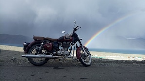 Een motorfiets op het strand, met een regenboog op de achtergrond.