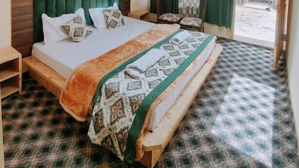 Een slaapkamer met een houten plafond, een bed met beddengoed met een patroon, groene gordijnen en uitzicht op buiten.