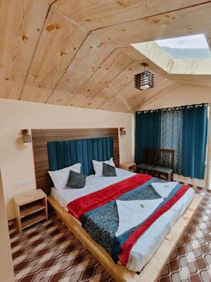 Un dormitorio con techo de madera, una cama con colcha roja y azul, y vistas al exterior.