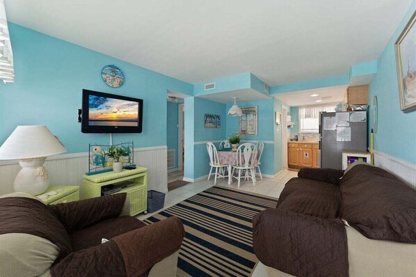 A living room with a TV, sofa, dining table, and kitchen area.