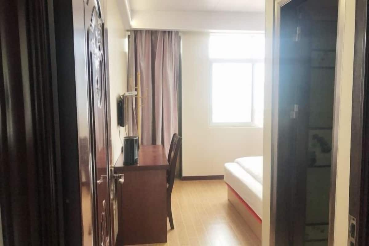 A hotel room with a bed, a desk, and a chair. There is a window providing natural light.