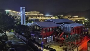A hotel with a prominent tower, a covered outdoor area with seating, and a well-lit building in the background. - Golden Bay 38 Homestay (Cangnan)