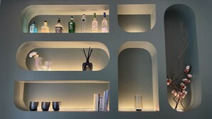 A wall with multiple shelves displaying various bottles and a few decorative items. - Luxueux Studio Cosy à Bastille (Paris)