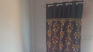 A single bed with white bedding, a dark headboard, and a floral curtain. - Maheshwari Homestay By GRB (Jamwa Ramgarh)