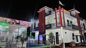 A modern building with a red and white facade, balconies, and a flag on top. - Maheshwari Homestay By GRB (Jamwa Ramgarh)