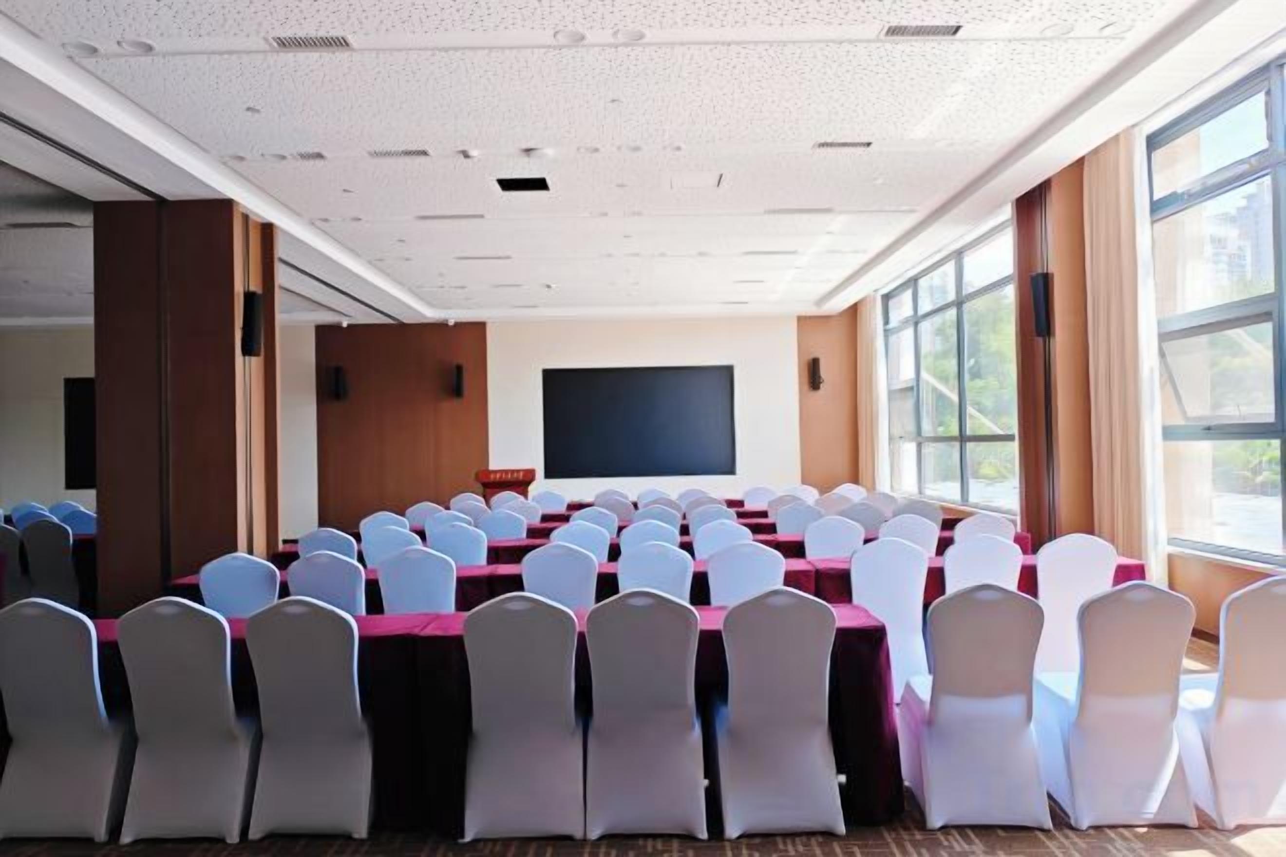 A conference room with rows of tables and chairs, a projector screen, and large windows.