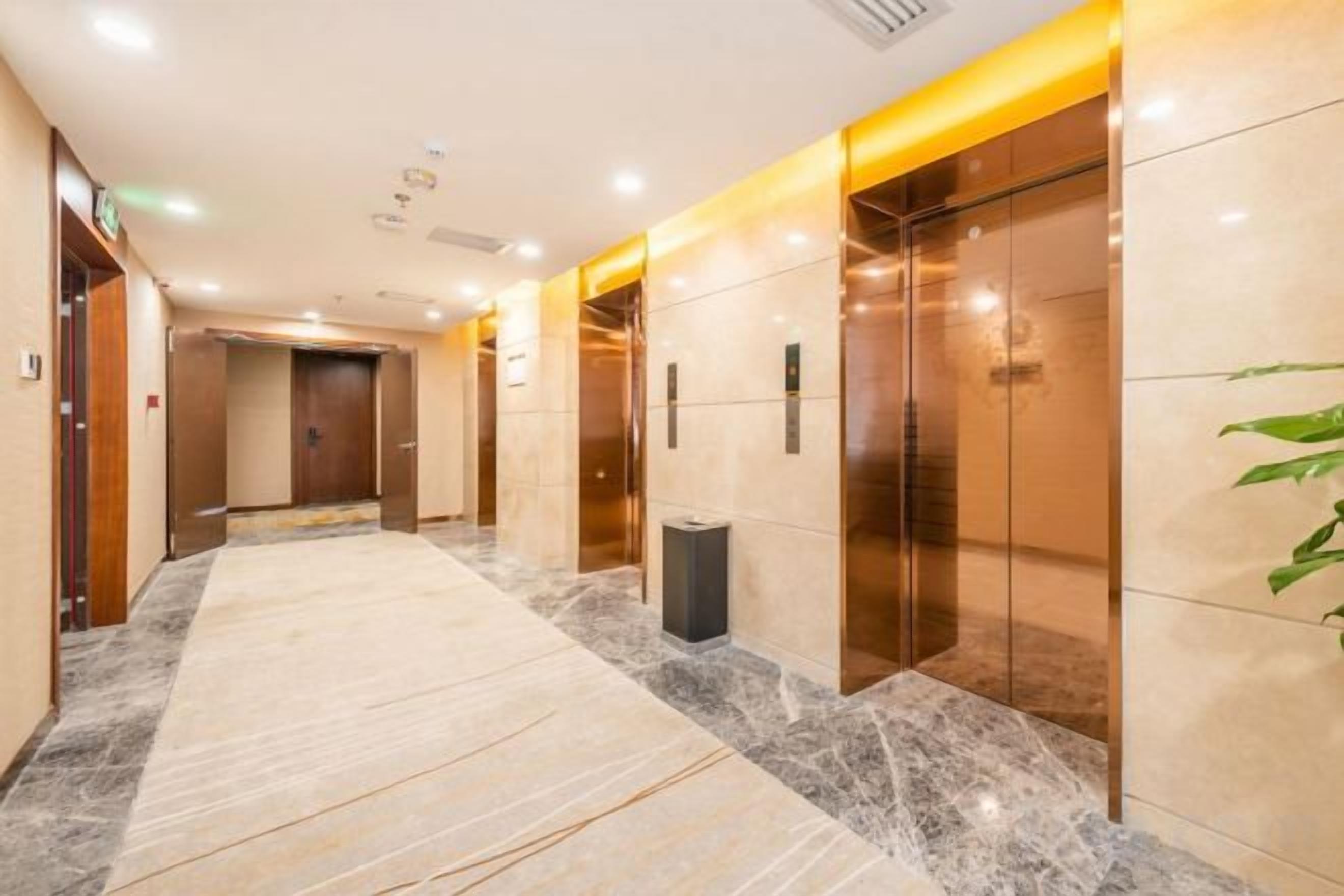 A hotel corridor with marble flooring, elevators, and a trash bin.