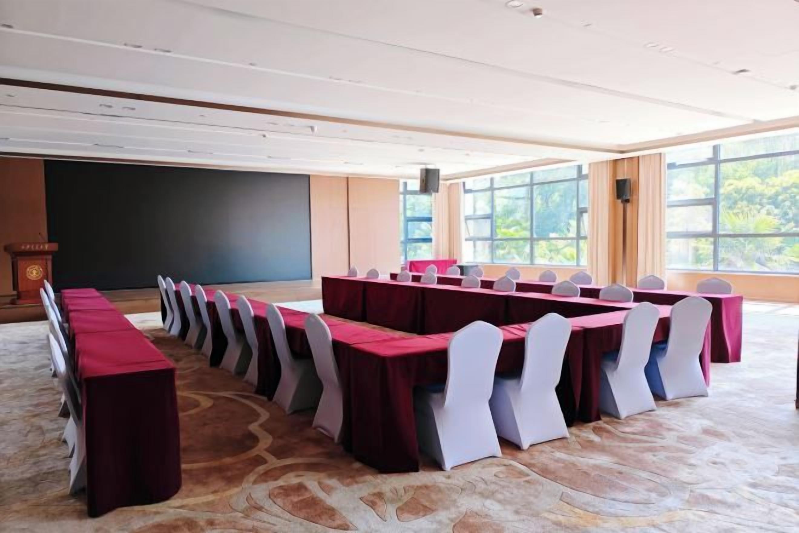 Un salón de conferencias con largas mesas y sillas, un atril y una pantalla grande.